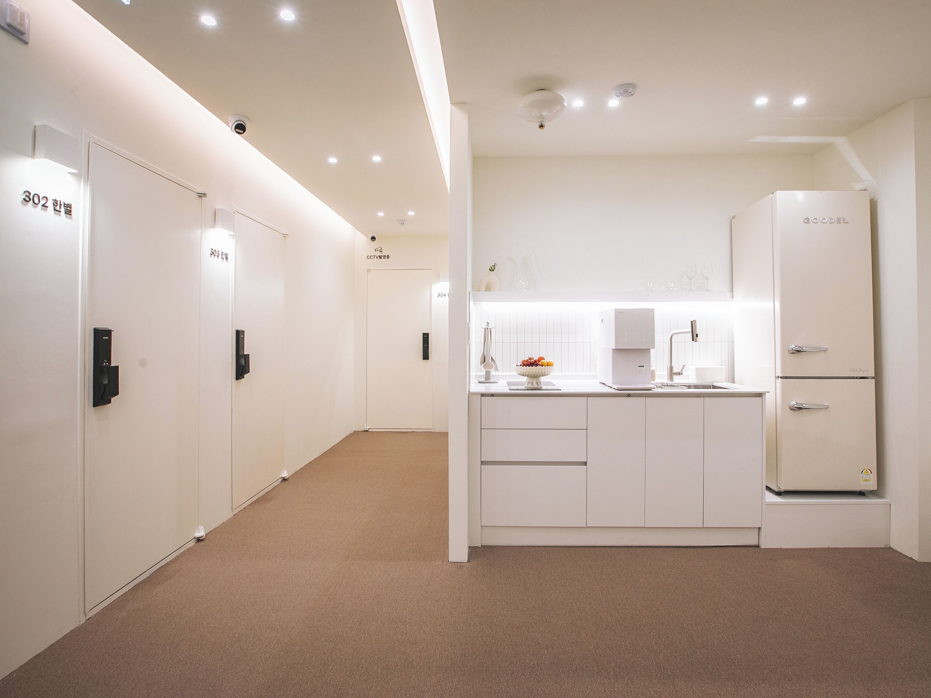 A modern, minimalist hotel room with a kitchenette, a large mirror, and a door with a number indicating the room.