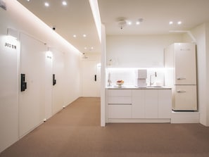 A modern, minimalist hotel room with a kitchenette, a large mirror, and a door with a number indicating the room.