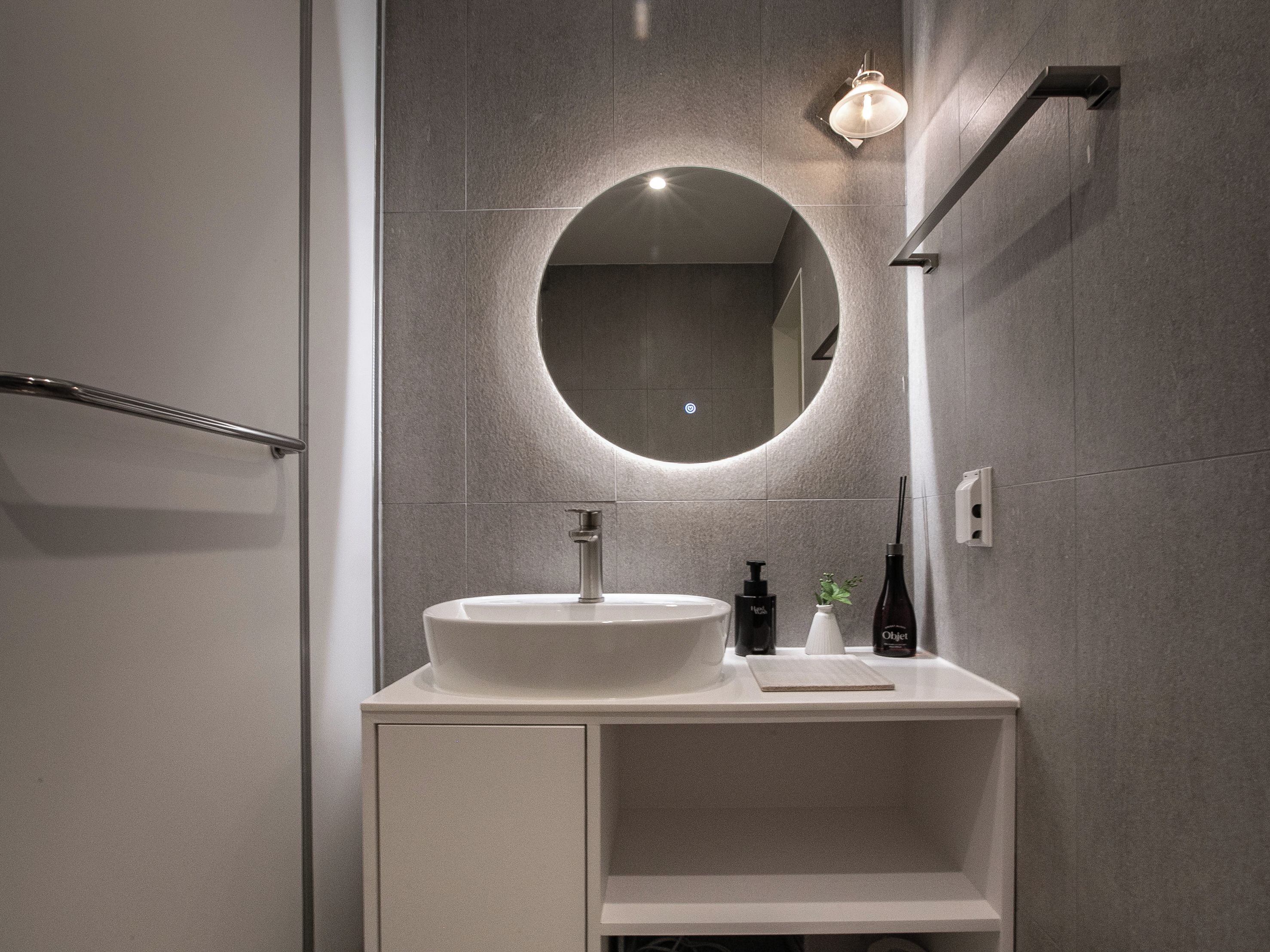 A modern bathroom with a round mirror, a white sink, and a towel rack.