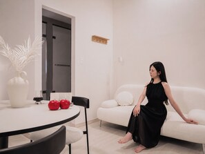 A modern living room with a white sofa, a dining table with chairs, and a vase with red apples.