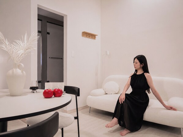 Una sala de estar moderna con un sofá blanco, una mesa de comedor con sillas y un florero con manzanas rojas.
