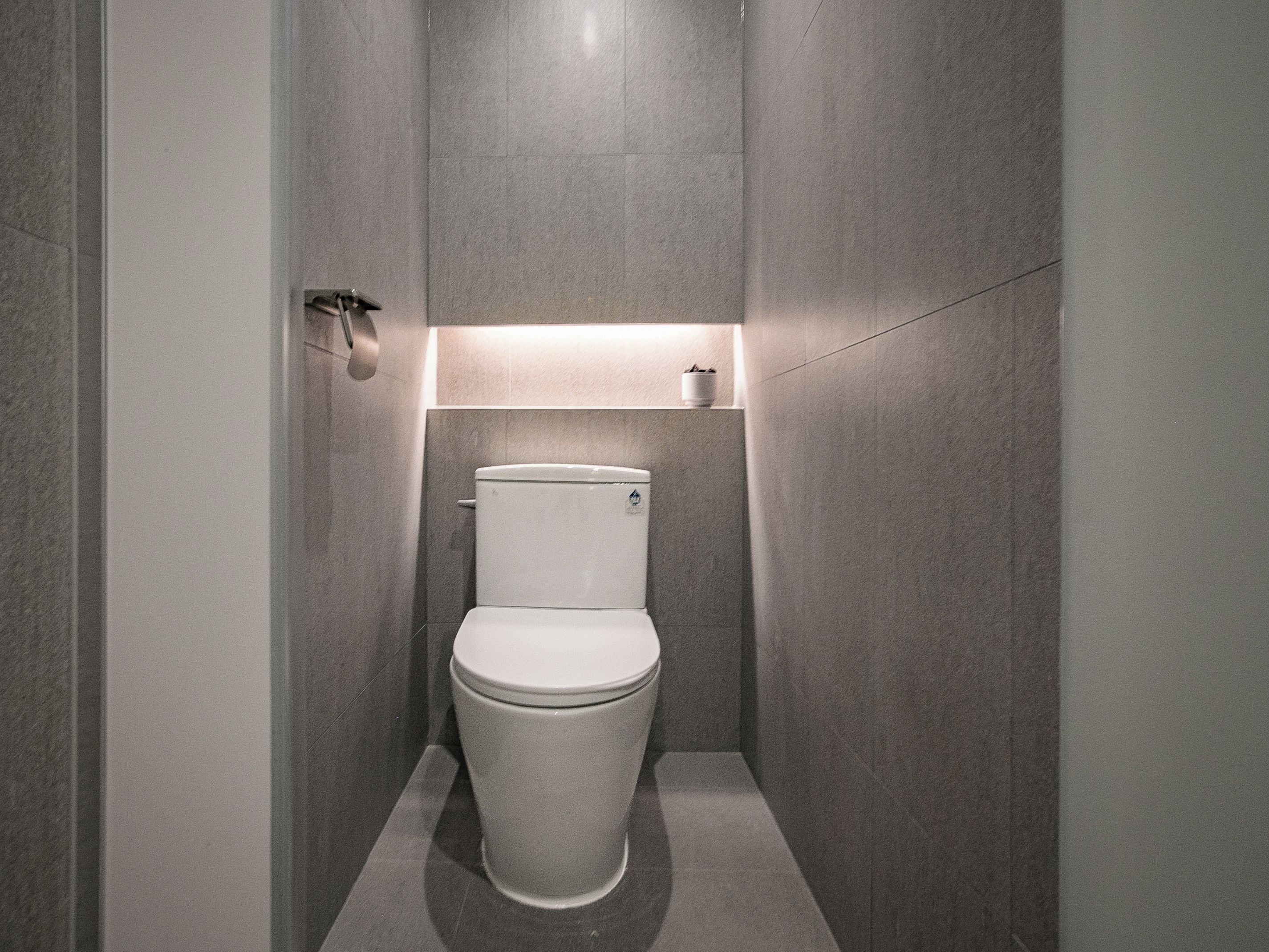 Un baño moderno con inodoro, repisa en la pared e iluminación.