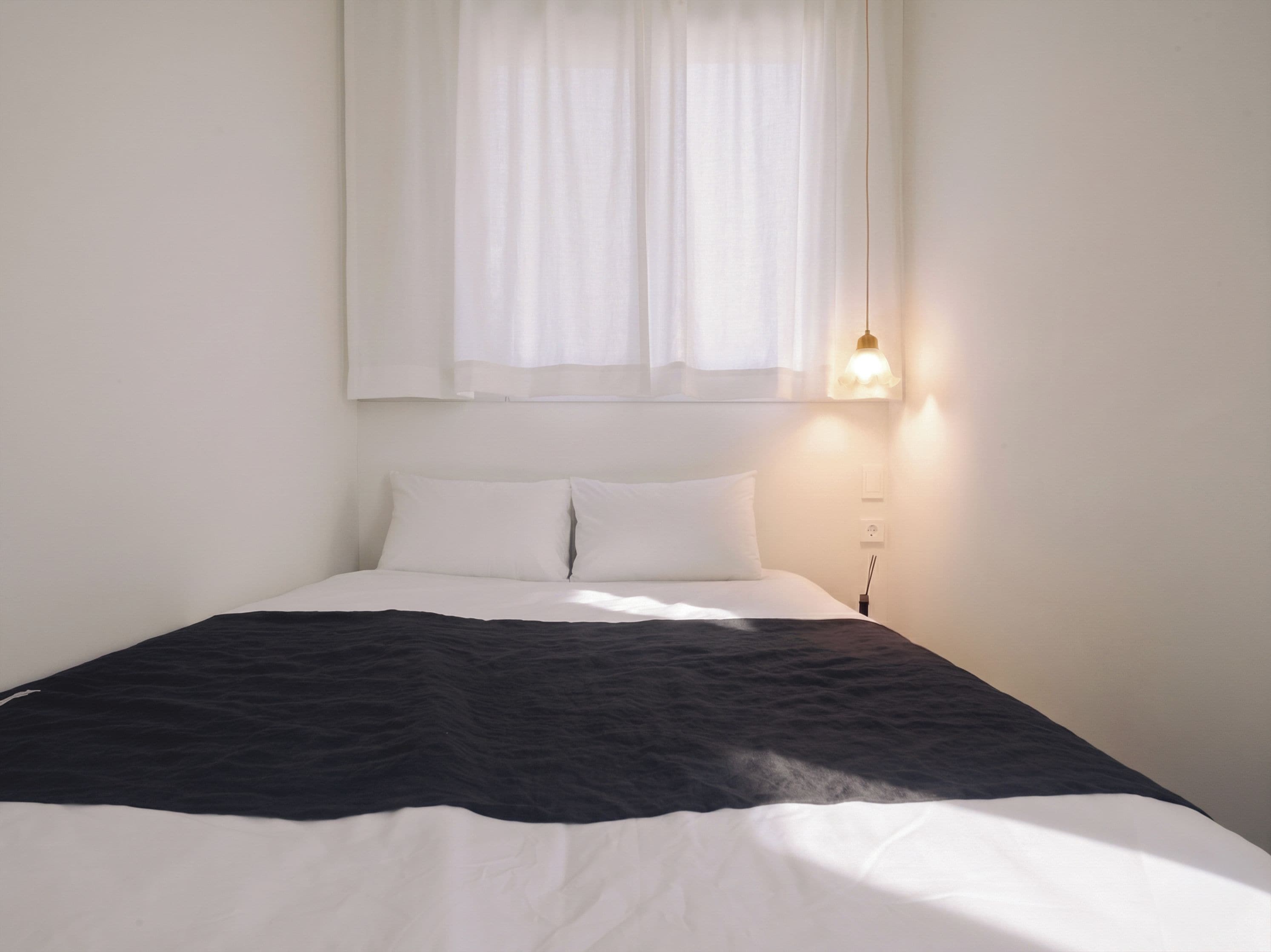 A bed with white and black bedding, a bedside lamp, and a window with sheer curtains.