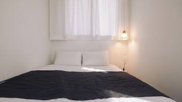 A bed with white and black bedding, a bedside lamp, and a window with sheer curtains.