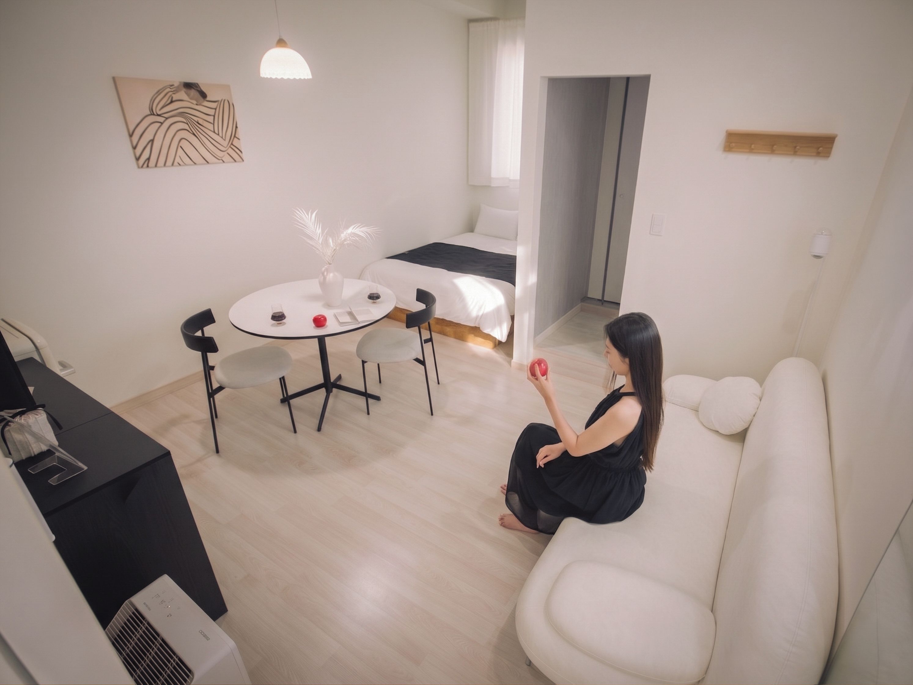 A modern living room with a white sofa, a dining table with chairs, and a small kitchen area with a refrigerator.