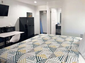 Ein Hotelzimmer mit Bett, Schreibtisch, Stuhl, Fernseher, Kühlschrank und Kleiderschrank.