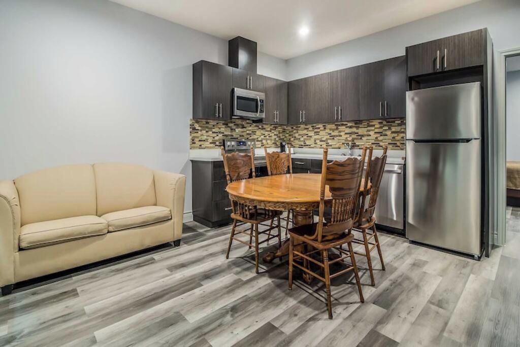 A modern kitchen with dark cabinets, a stainless steel refrigerator, and a wooden dining table with chairs.