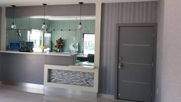 Un área de recepción con mostrador, espejo, lámparas colgantes y una puerta, además de una pared con diseño.