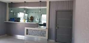 A reception area with a counter, a mirror, hanging pendant lights, a door, and a patterned wall.