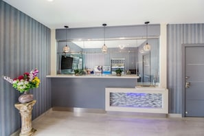 A reception area with a modern design, featuring a reception desk, a decorative vase with flowers, and a tiled accent wall. - 2 Queen Suite w/ Kitchen & Free Parking l Travel Easy with Your Pet by Your Side (Deer Park)