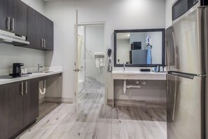 A modern kitchen with dark cabinets, a stainless steel refrigerator, and a glass shower enclosure.