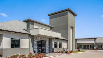A modern building with a flat roof, a central entrance with a stone facade, and a parking area with red lines.