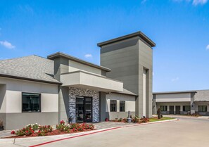 A modern building with a flat roof, a central entrance with a stone facade, and a parking area with red lines.