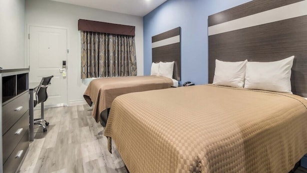 Ein Hotelzimmer mit zwei Betten, einem Schreibtisch, einem Stuhl, einem Kleiderschrank und einem Fenster mit Vorhängen.