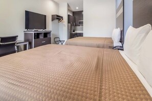 A hotel room with a bed, a TV, a desk, and a kitchenette.