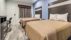 Ein Hotelzimmer mit zwei Betten, einem Schreibtisch, einem Stuhl, einem Kleiderschrank und einem Fenster mit Vorhängen.
