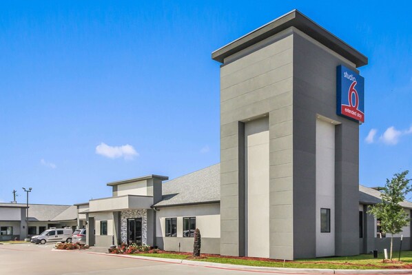 A modern hotel building with a prominent 'studio 6' sign, a parking lot, and a well-maintained lawn.