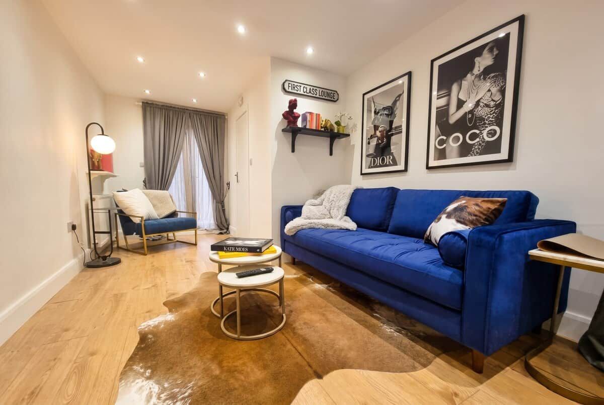 A living room with a blue sofa, a coffee table, a lamp, and a rug. There are books on the coffee table and a remote control.