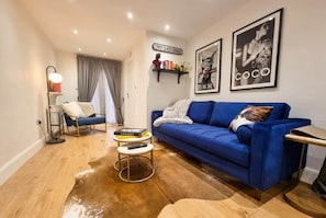 A living room with a blue sofa, a coffee table, a lamp, and a rug. There are books on the coffee table and a remote control. - East Dulwich 2BR Flat w/ Garden & Driveway Parking (London)