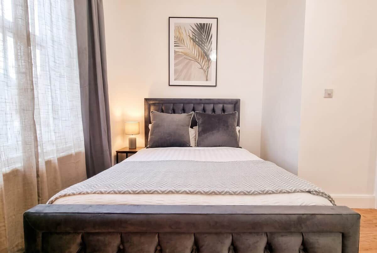 Een slaapkamer met een bed, gordijnen, een nachtkastje, een lamp en een lijst met een foto aan de muur.
