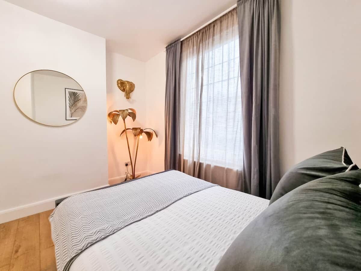 Une chambre à coucher avec un lit, un miroir rond et une fenêtre avec des rideaux.