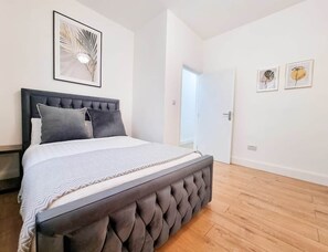 Ein Schlafzimmer mit einem großen Bett, einer Tür und einer Wand mit gerahmten Kunstwerken.