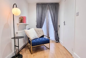 A corner room with a blue upholstered chair, a floor lamp, a radiator, and a window with curtains. - East Dulwich 2BR Flat w/ Garden & Driveway Parking (London)