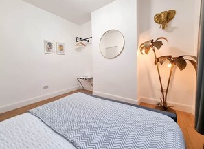 A bedroom with a bed, a round mirror, wall art, a floor lamp, and a small folding chair. - East Dulwich 2BR Flat w/ Garden & Driveway Parking (London)