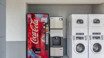 Máquina expendedora con el logotipo de Coca-Cola, dispensador de agua y una pila de lavadoras.