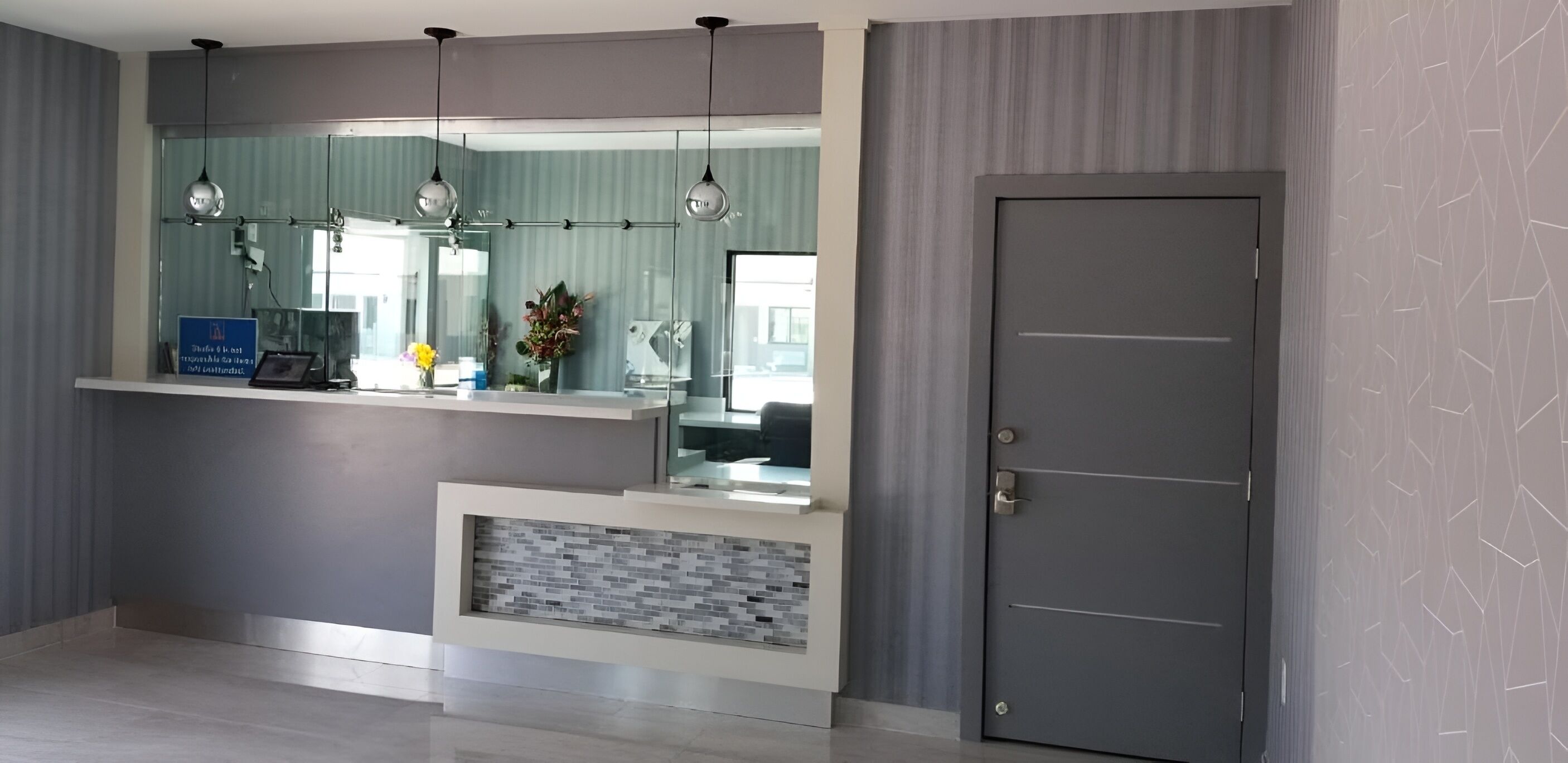 A reception area with a counter, a mirror, hanging pendant lights, a door, and a patterned wall.
