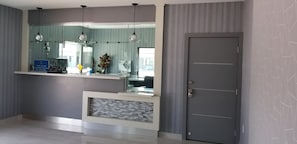 A reception area with a counter, a mirror, hanging pendant lights, a door, and a patterned wall.