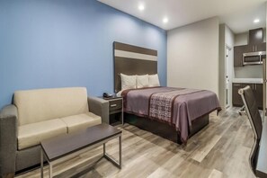 A bedroom with a bed, a nightstand, a sofa, a small table, and a kitchenette with a microwave.