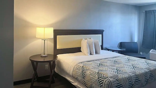 A hotel room with a bed, a bedside lamp, a chair, and a small table. - Studio King Unit | Close to Hutchinson County Museum - 0.9 miles (Borger)