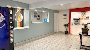 A hotel lobby with a vending machine, a reception desk, a coffee machine, and a potted plant.