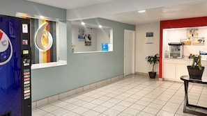 Un hall d’hôtel comprenant un distributeur automatique, un comptoir de réception, une machine à café et une plante en pot.
