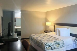 A hotel room with a bed, bedside table, lamp, and a desk with a computer. - Studio King Unit | Close to Hutchinson County Museum - 0.9 miles (Borger)
