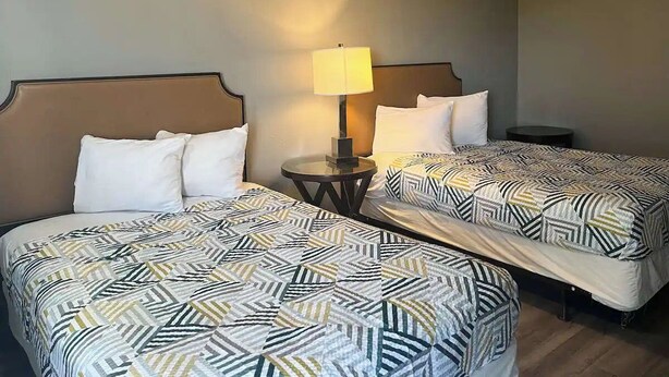 A hotel room with two beds, each with a patterned bedspread, a bedside table with a lamp, and a small round table. - Pet-Friendly Unit w/ 2 Queen Beds | 12 Min Walk to Frank Phillips College (Borger)