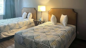 A hotel room with two beds, each with a patterned bedspread, a bedside table with a lamp, and a window with curtains. - Pet-Friendly Unit w/ 2 Queen Beds | 12 Min Walk to Frank Phillips College (Borger)