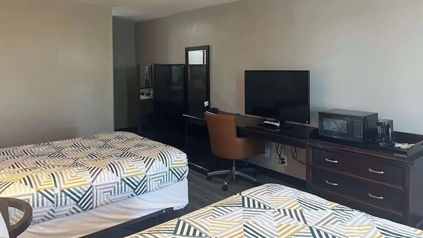 A hotel room with two beds, a desk, a chair, a television, and a microwave.