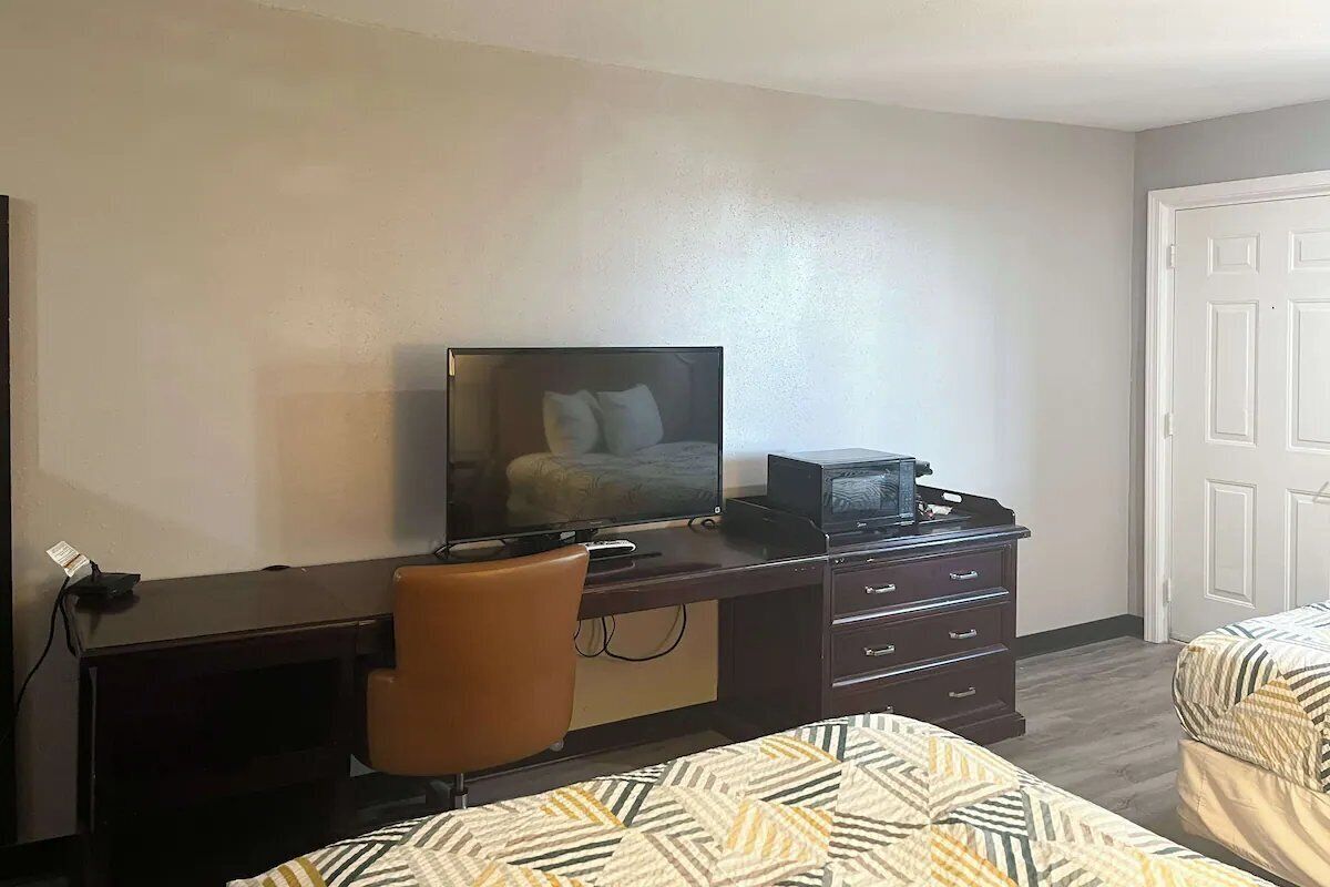 A hotel room with a desk, a television, a chair, and two beds.