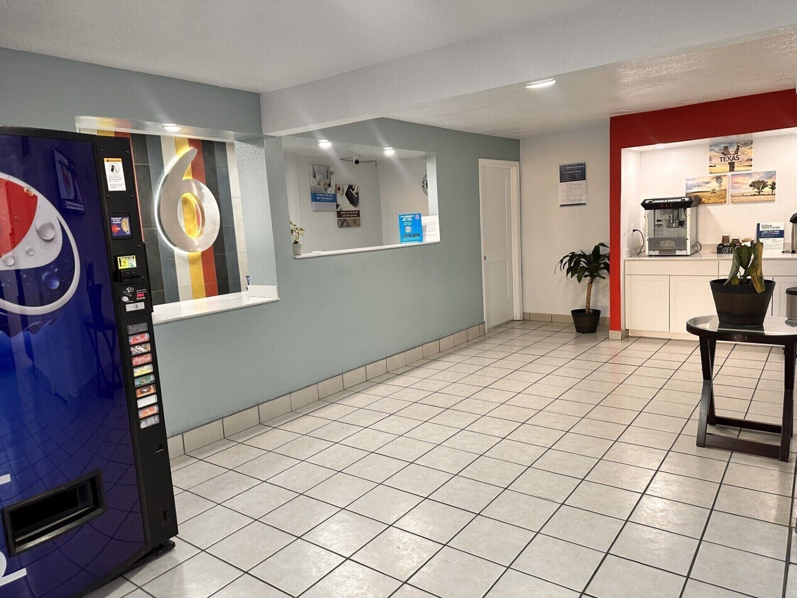 A hotel lobby with a vending machine, a reception desk, a coffee machine, and a potted plant.