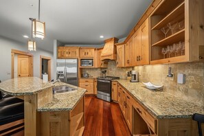 Eine moderne Küche mit Granit-Arbeitsplatten, Holzschränken, Edelstahlgeräten und einem integrierten Weinkühlschrank.