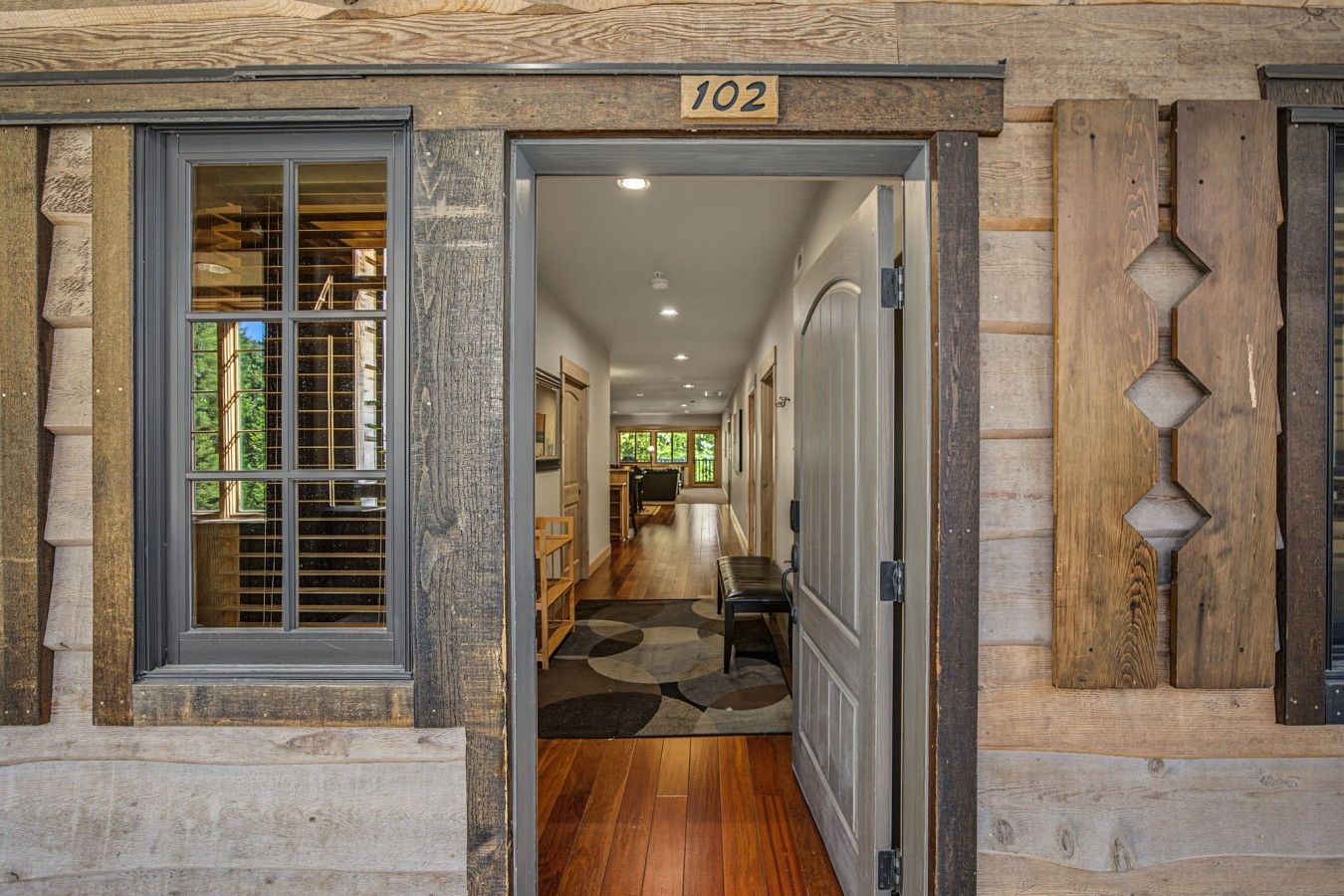A hallway with a wooden door labeled '102' leading to a room with a window and a bench.
