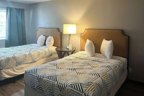 Une chambre d’hôtel avec deux lits, chacun recouvert d’une couvre-lit à motifs, une table de chevet avec une lampe et une fenêtre avec des rideaux.