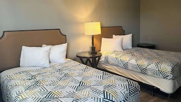 Habitación de hotel con dos camas, cada una con cubrecama estampado, una mesita de noche con lámpara y una pequeña mesa redonda.