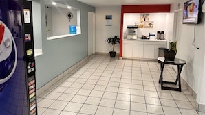 A hotel lobby with a vending machine, a potted plant, a coffee machine, and a television on the wall.