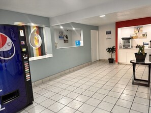 A hotel lobby with a vending machine, a reception desk, a coffee machine, and a potted plant.