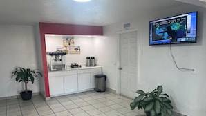 A small kitchenette with a coffee machine, a trash bin, and a television displaying a weather forecast.