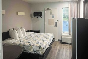 Habitación de hotel con cama, mesita de noche, pequeño escritorio, una silla, ventana con cortinas y puerta con aviso.