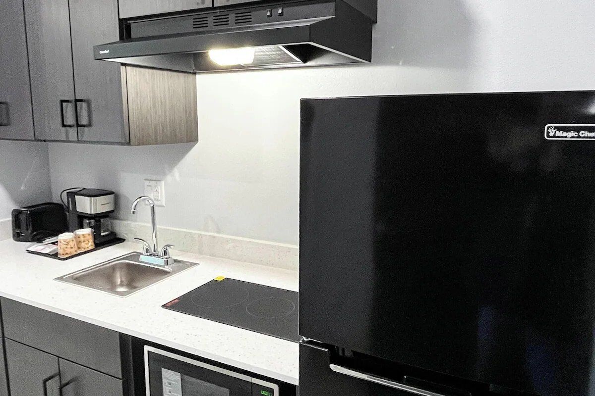 Una cocina con un refrigerador negro, un lavamanos de acero inoxidable y una cafetera.